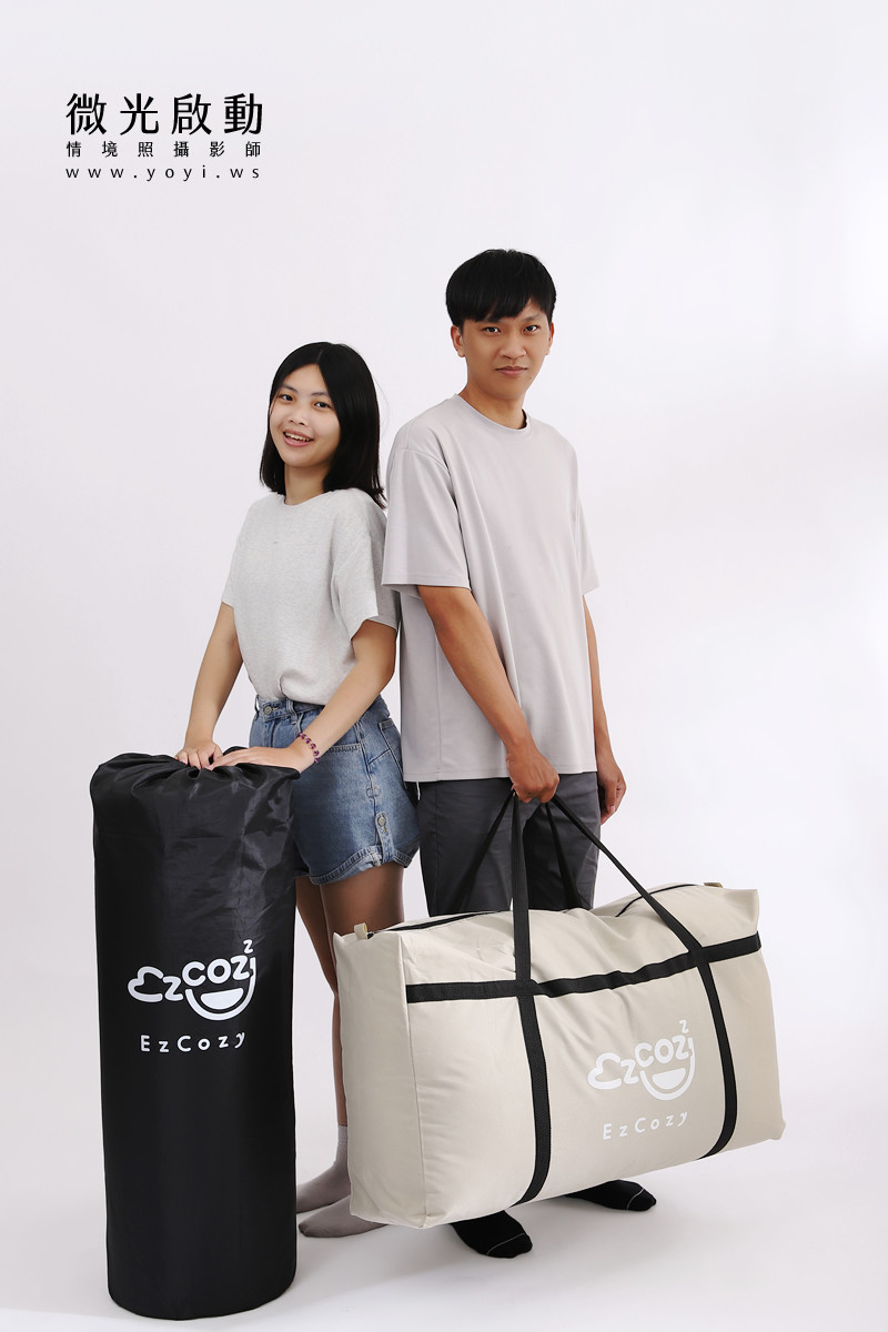 專業攝影服務作品。一對年輕情侶在白色背景前，展示可收納的黑色和米白色寢具。強調寢具攝影、商品攝影、攝影專案。