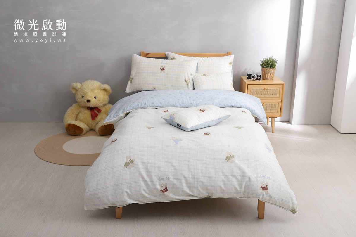 居家商品攝影作品。在舒適臥室場景中，以淺藍色和白色格紋的寢具布置，營造溫馨感。突出寢具攝影、商品攝影、專業攝影。