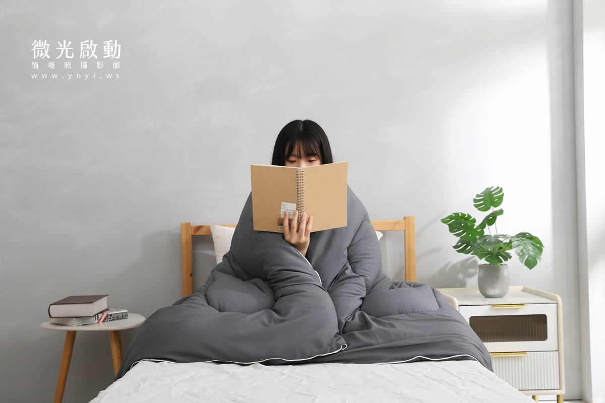 居家商品攝影。一位模特兒將白色棉被蓋在身上，展現其保暖與舒適感。適用於寢具攝影、攝影服務、專業攝影。