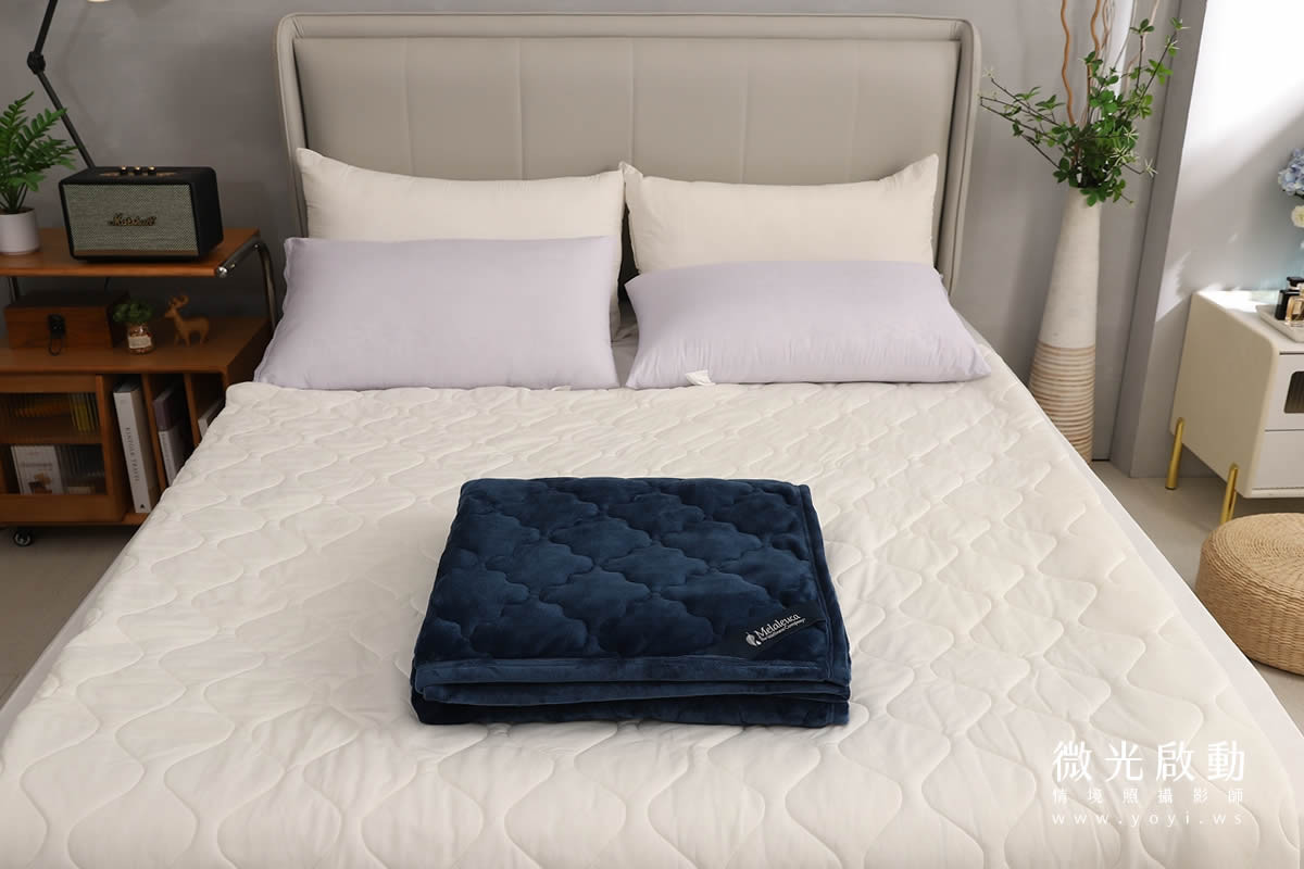 深藍色絎縫毛毯摺疊置於白色床單上，視覺焦點集中，簡約專業的商品攝影