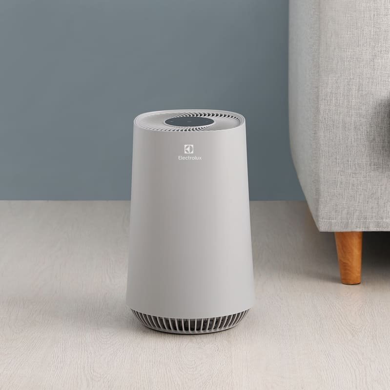 現代錐形灰色伊萊克斯空氣清淨機的全景照片,擺放在一張淺灰色沙發旁邊。